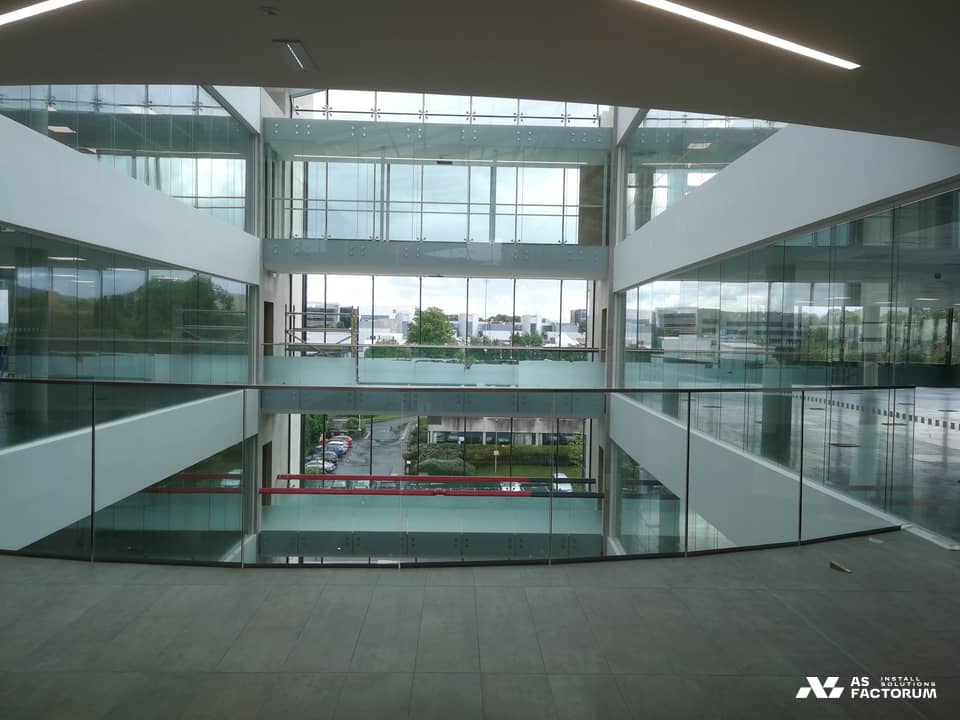 Atriu luminos al unei clădiri moderne cu mai multe etaje, cu pereți vitrați și balustrade din sticlă