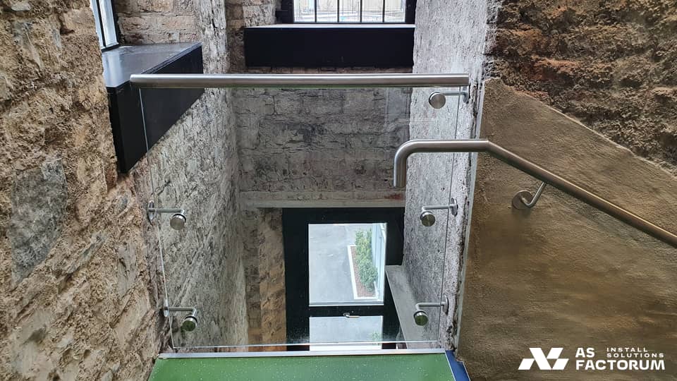 Glass balustrade with stainless handrail at a stairwell opening in a stone building