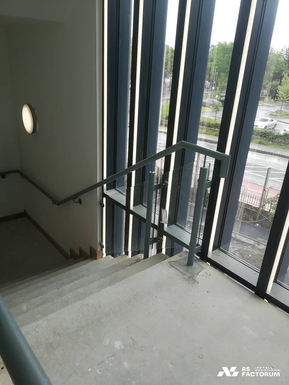 Stairwell with a glass balustrade and metal handrail beside a glazed wall