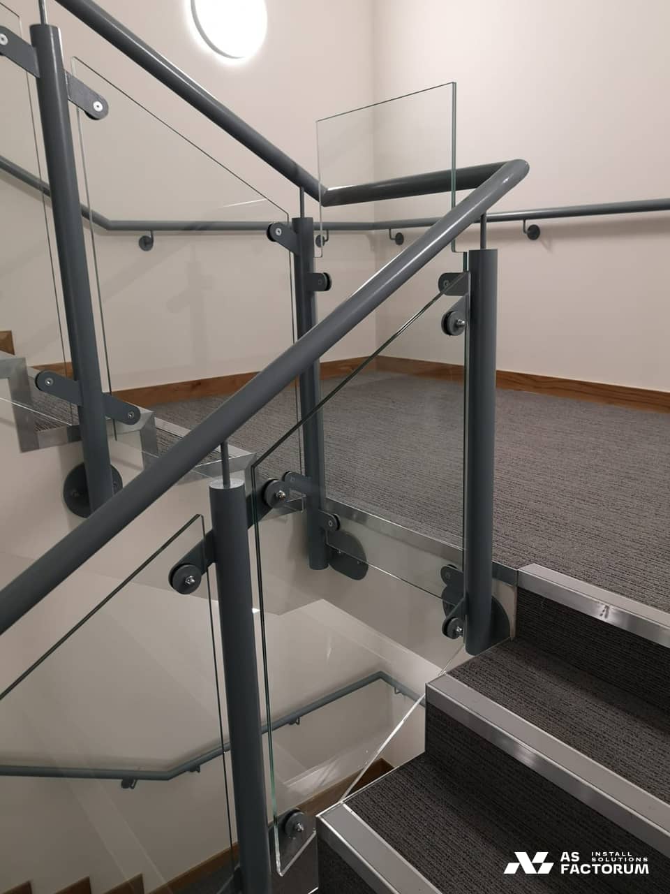 Detail of a glass balustrade fixed with metal clamps to steel posts beside a staircase