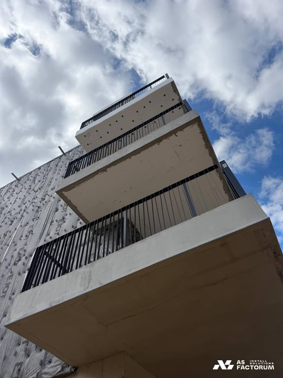 Vertical-bar metal railings installed along concrete balconies in front of a facade still being finished