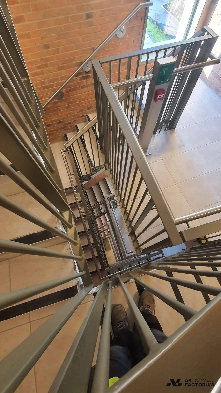 Looking down the stairwell void past a round-bar balustrade and stainless handrail