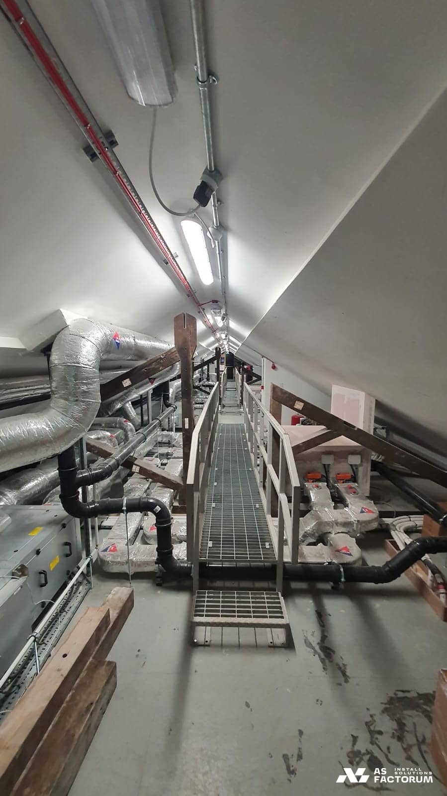 Grated walkway with railings in the roof void, running beside insulated ducts