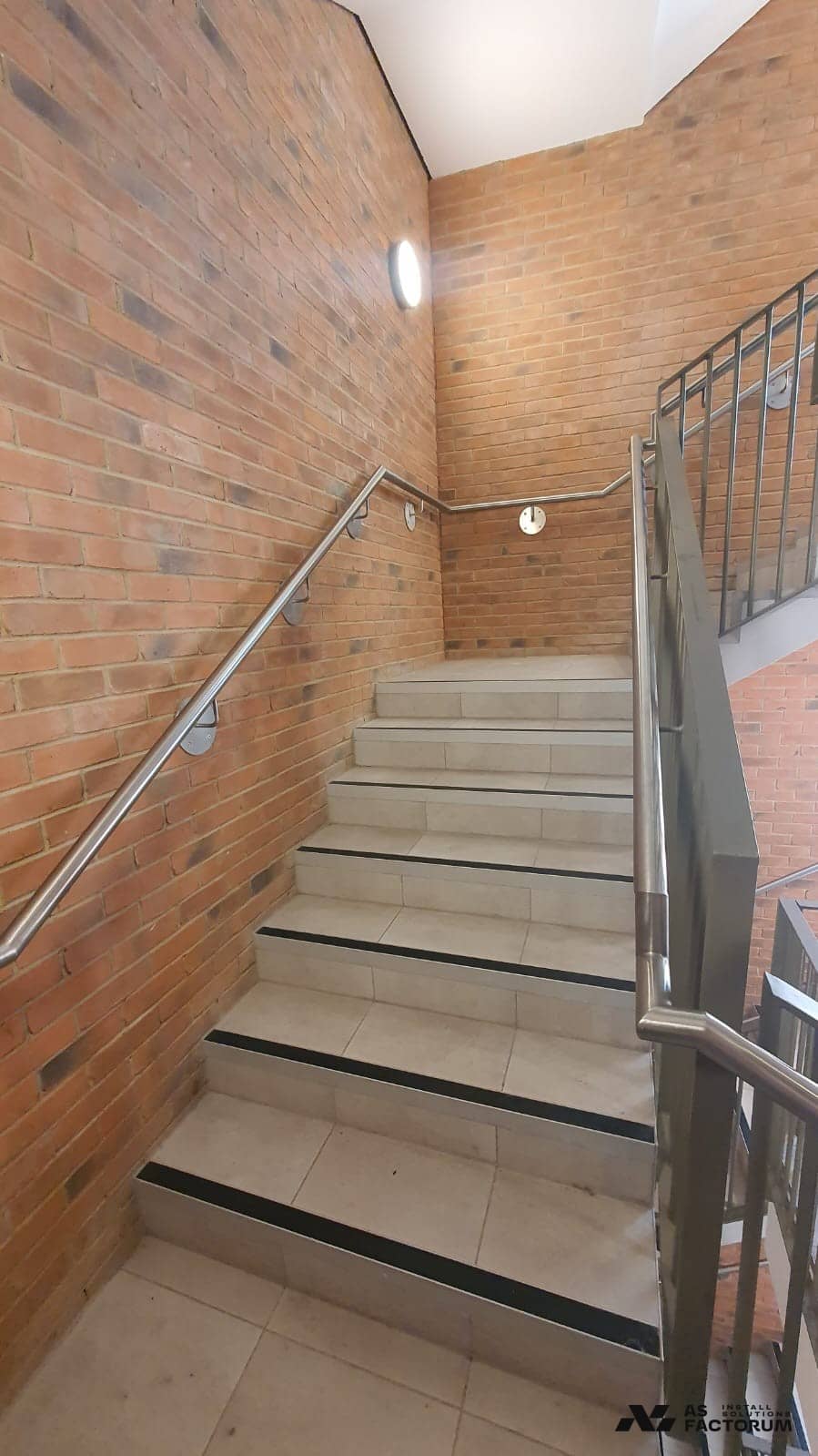 Stair flight with tiled steps and a metal balustrade fixed against a brick wall