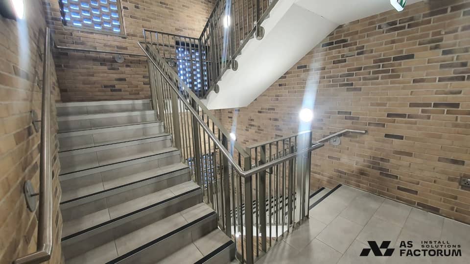 Successive stair flights between brick walls, with a painted steel balustrade and stainless handrail