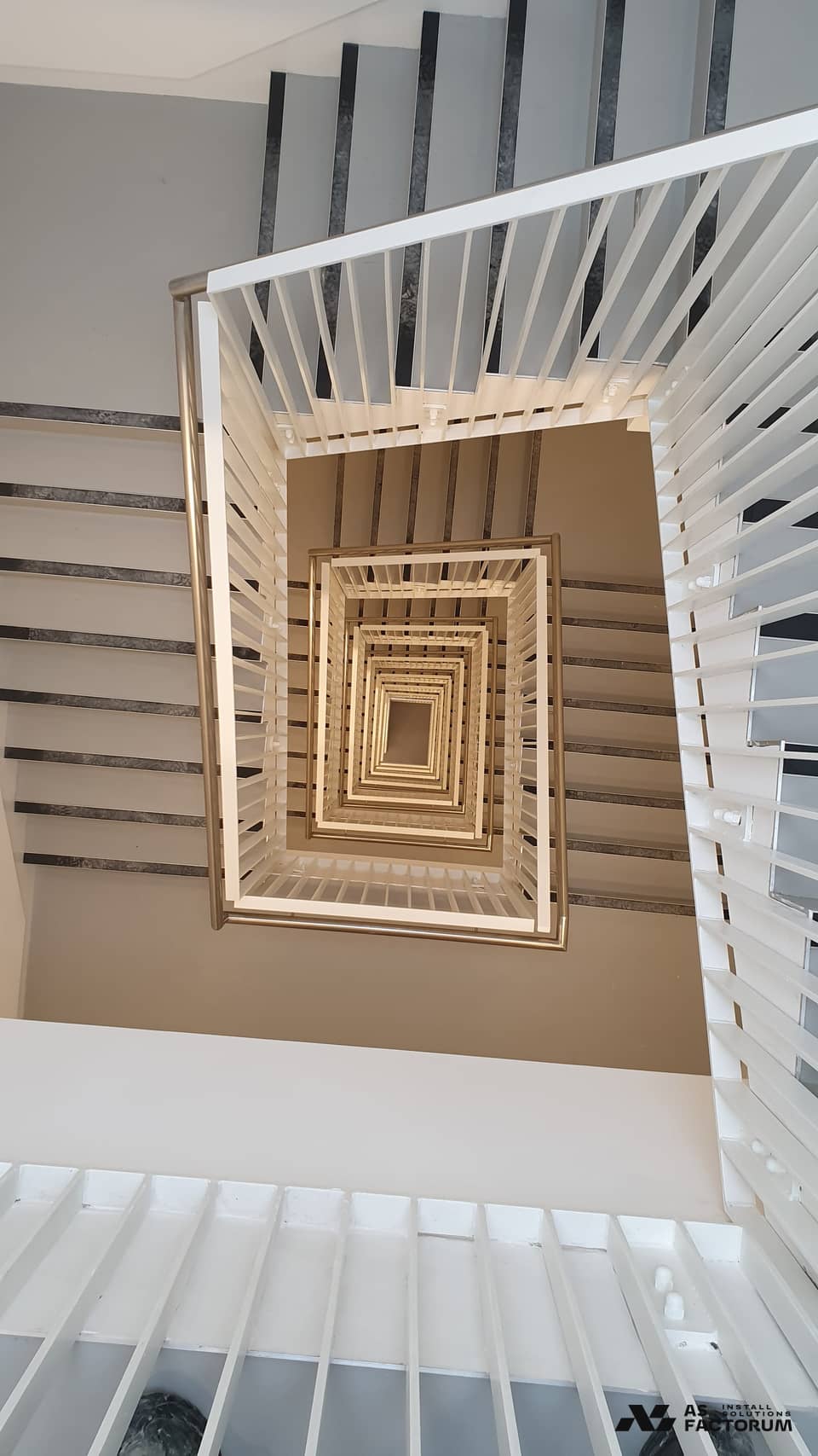 Stairwell seen from above, with a white slatted balustrade and metal handrail