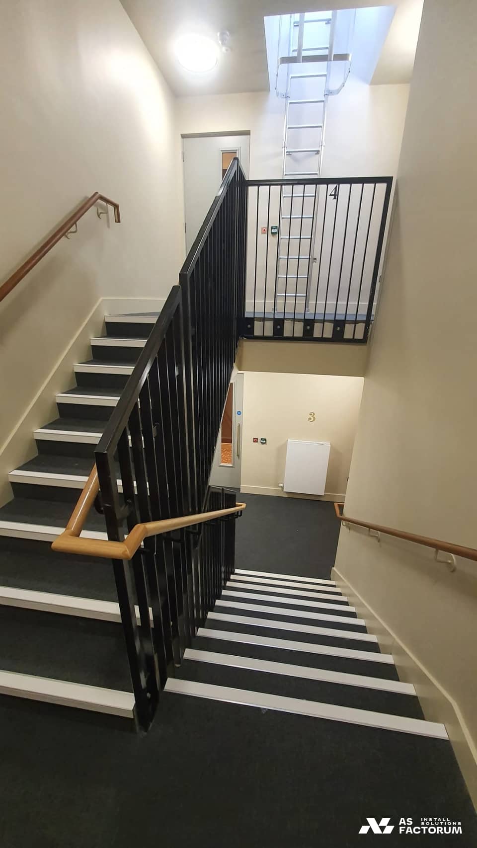 Interior staircase with a black metal balustrade and a fixed roof-access ladder at the top