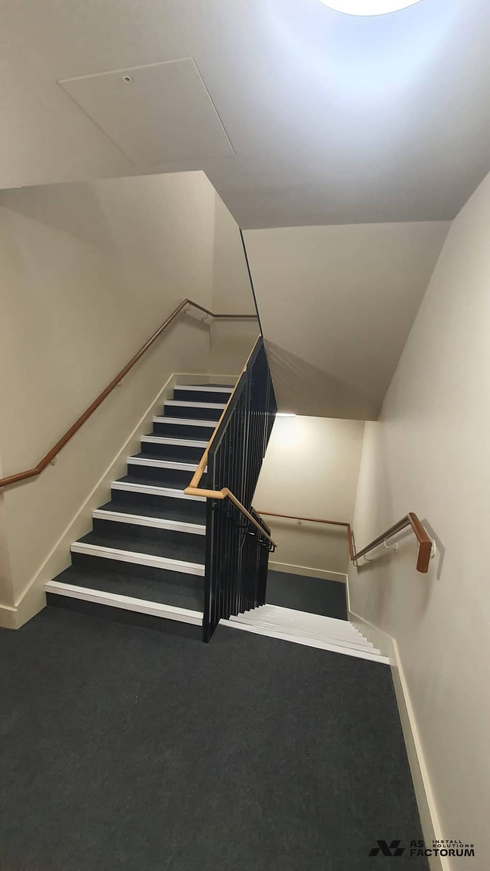 Interior stair flight with a black steel balustrade, timber handrail and dark carpeted steps