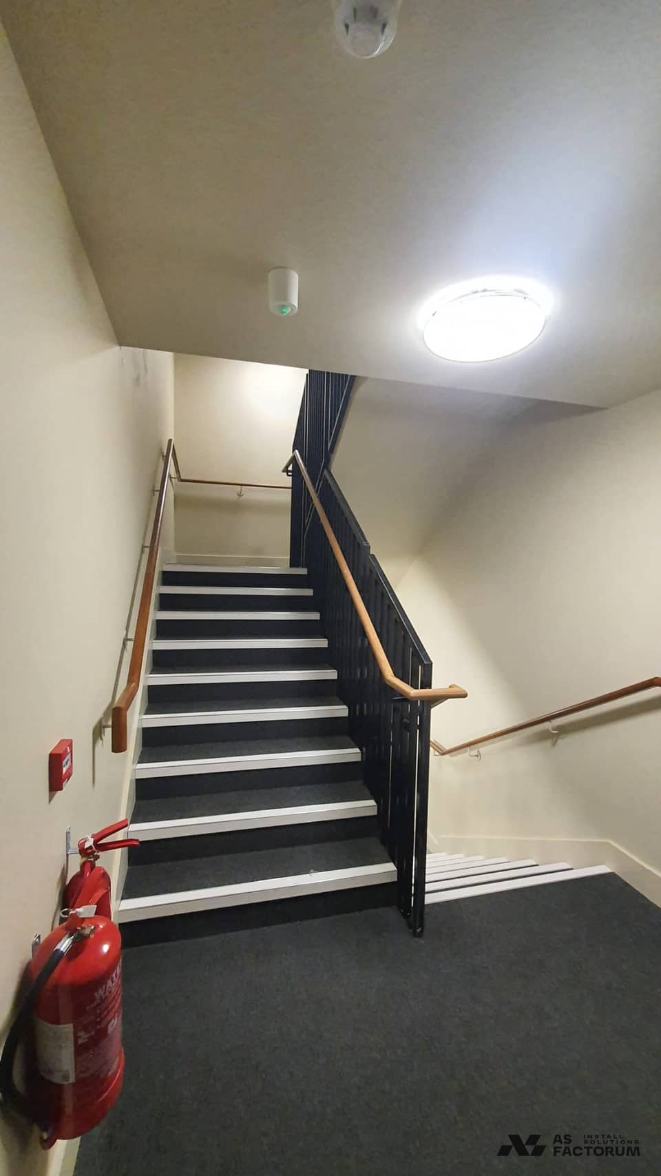 Interior stair with a black balustrade and timber handrail, and a fire extinguisher mounted on the wall