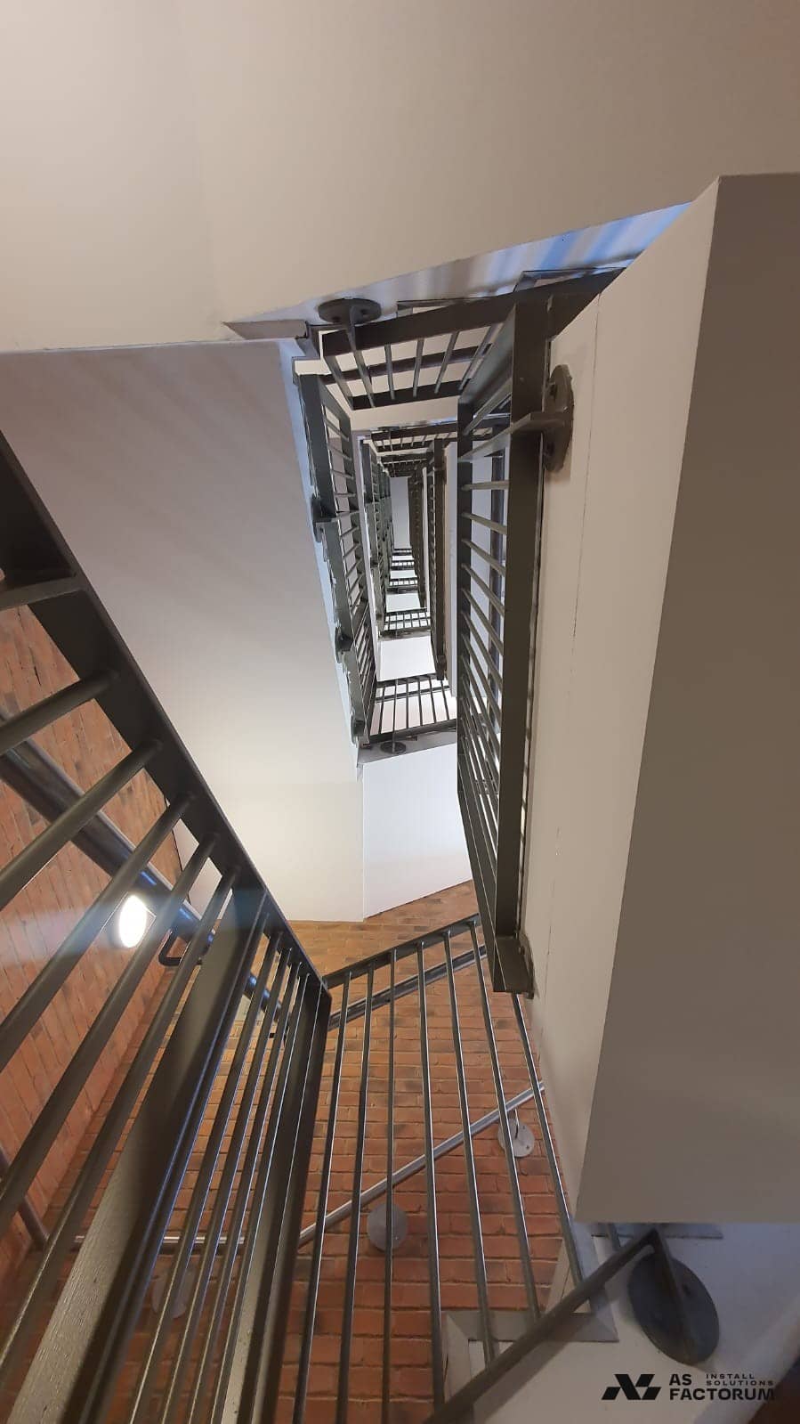 Upward view of a brick stairwell with stacked flights and metal balustrades