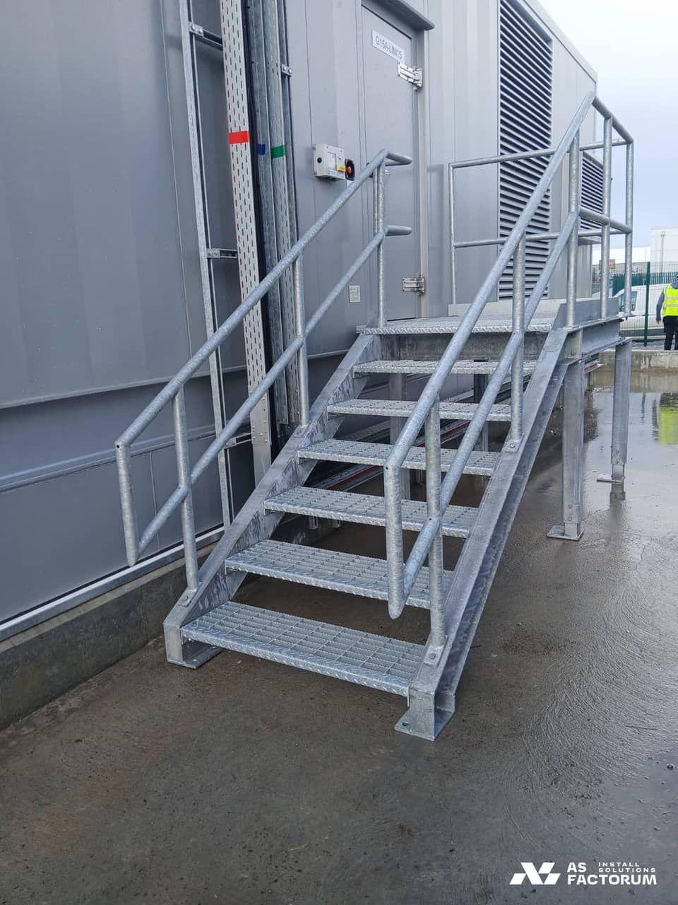 Galvanised stair with grating treads and a handrail leading up to a grey container
