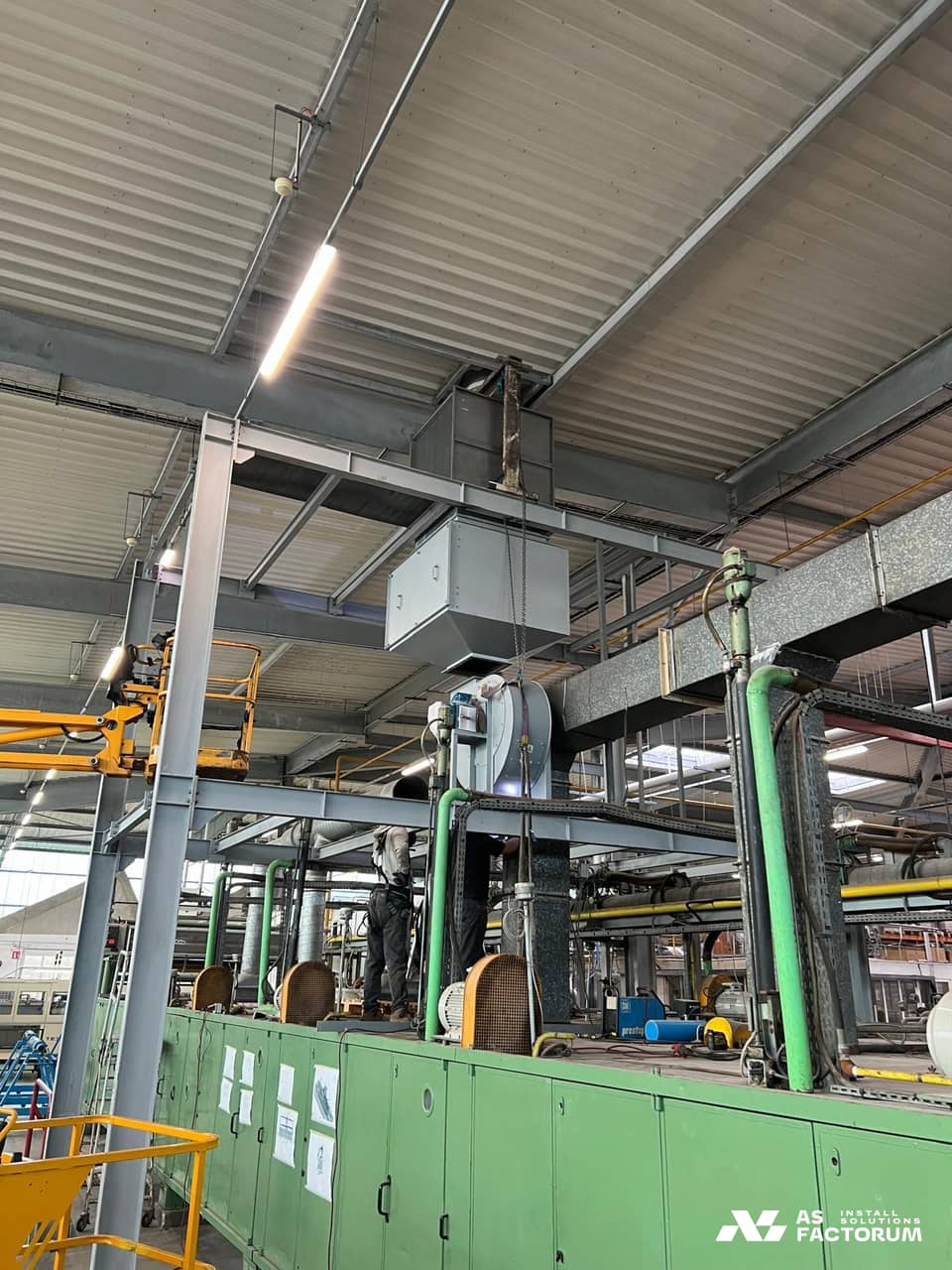 Steel structure carrying a fan housing above a green machine inside the hall