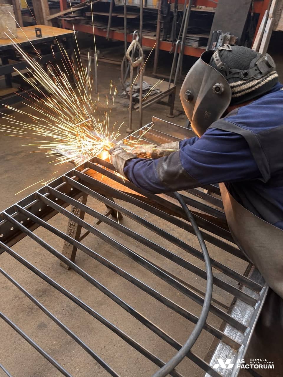 Welder in a protective mask grinding a steel bar grid, with sparks flying around