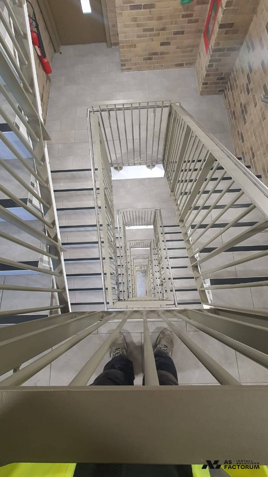 View down a stairwell with a round-bar balustrade and tiled steps with black nosings