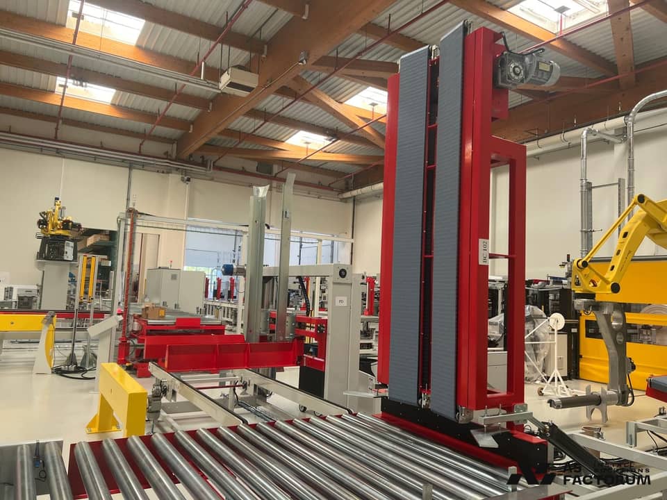 Red vertical conveyor lift with roller conveyors and a yellow robot behind
