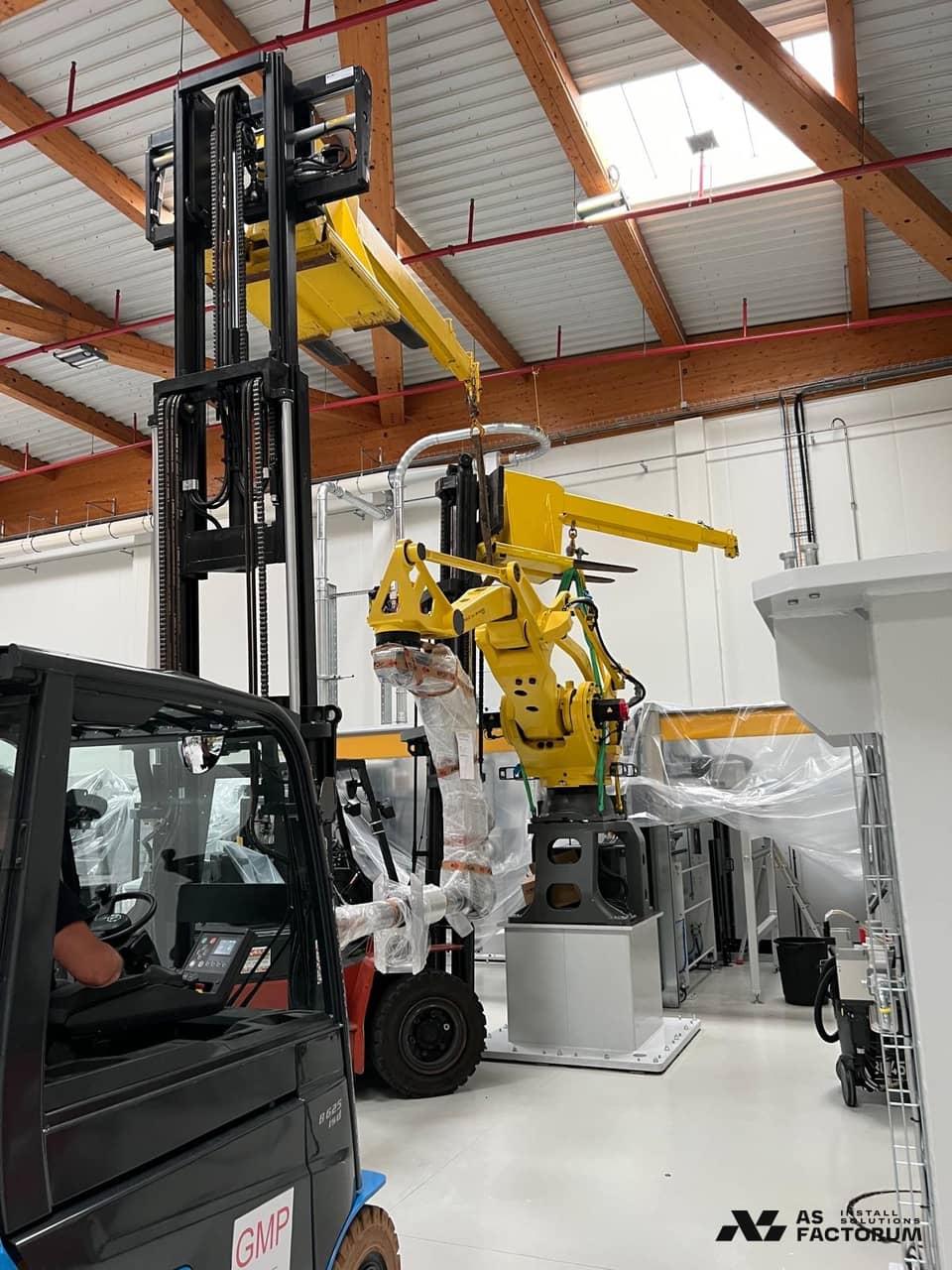 Yellow robot lifted by a forklift, with another forklift cab in the foreground