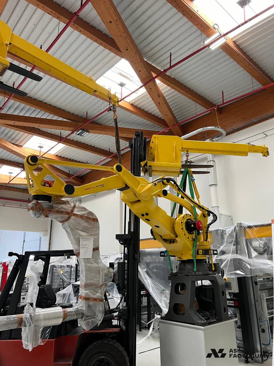 Yellow robot hanging from a forklift, with timber trusses visible behind it