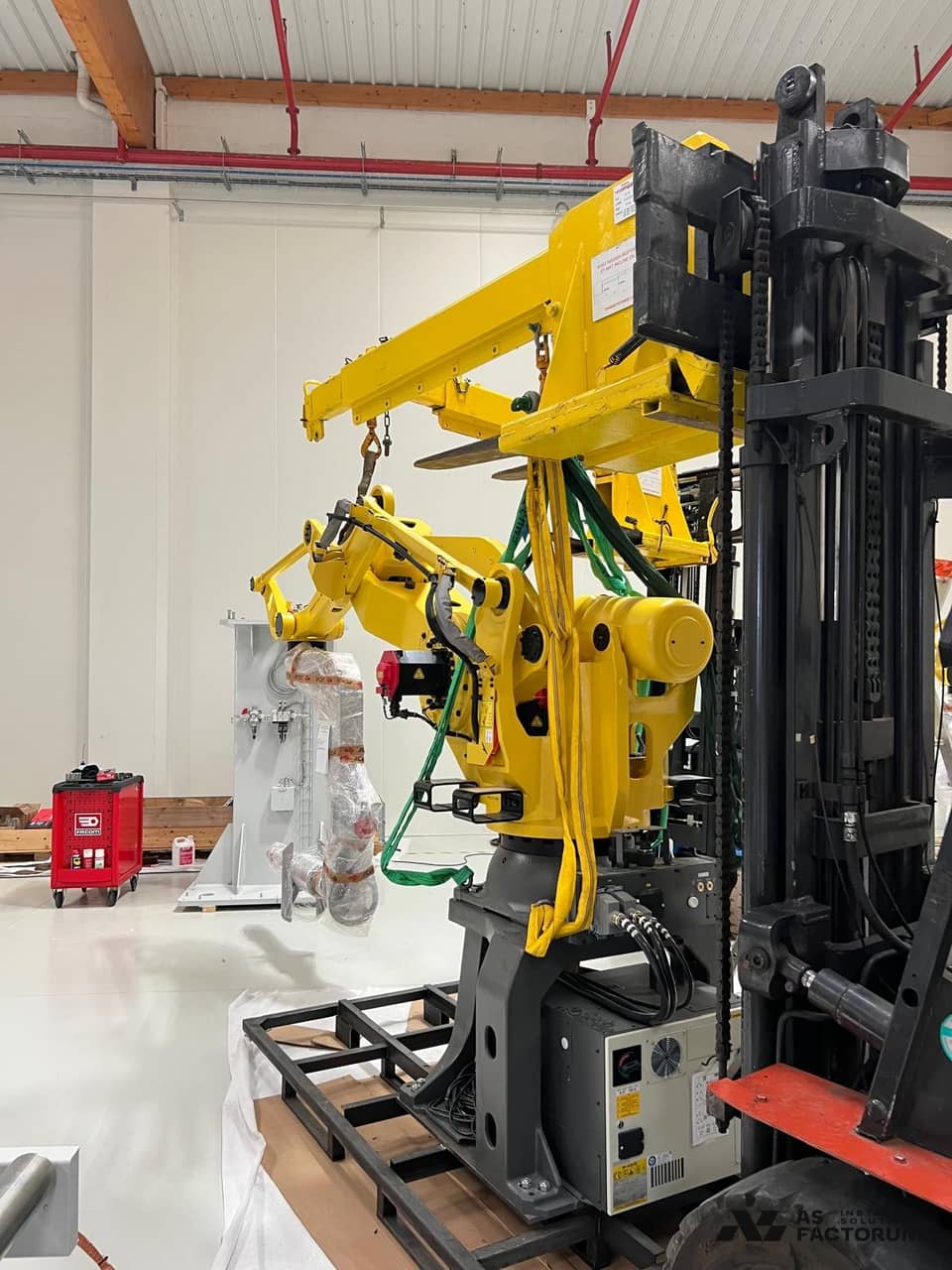 Side view of a yellow robot suspended from a forklift, its arm protected with wrapping