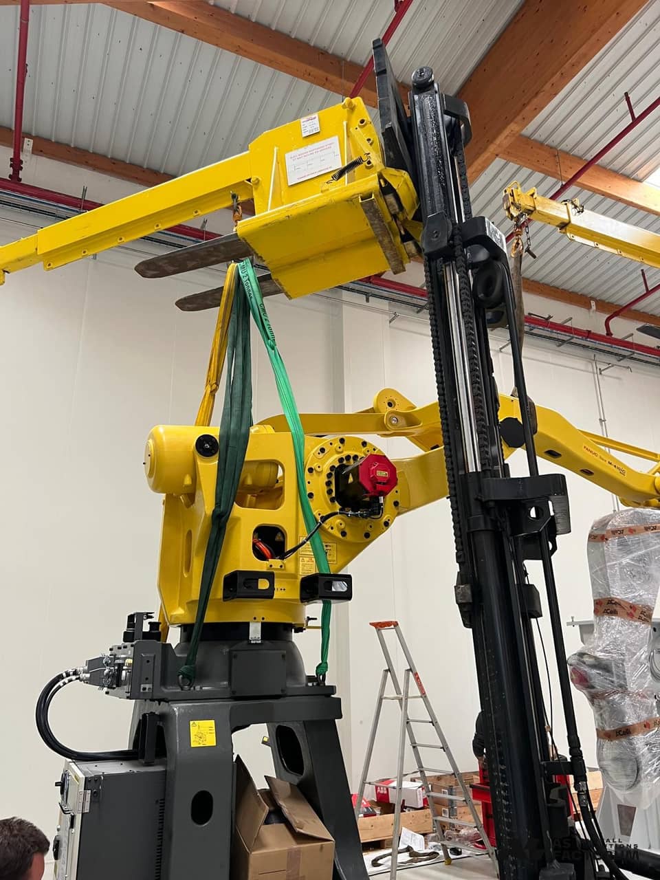 Close-up of lifting slings attached to a yellow industrial robot held by a forklift