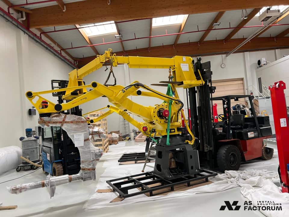 Yellow industrial robot on a pallet being prepared for installation, beside forklifts
