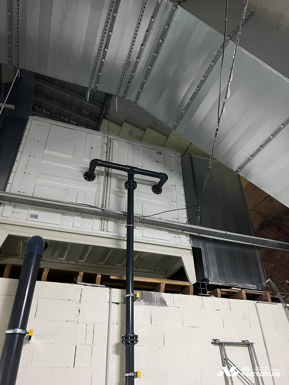Rectangular sheet-metal ducts above white access panels, with a black pipe