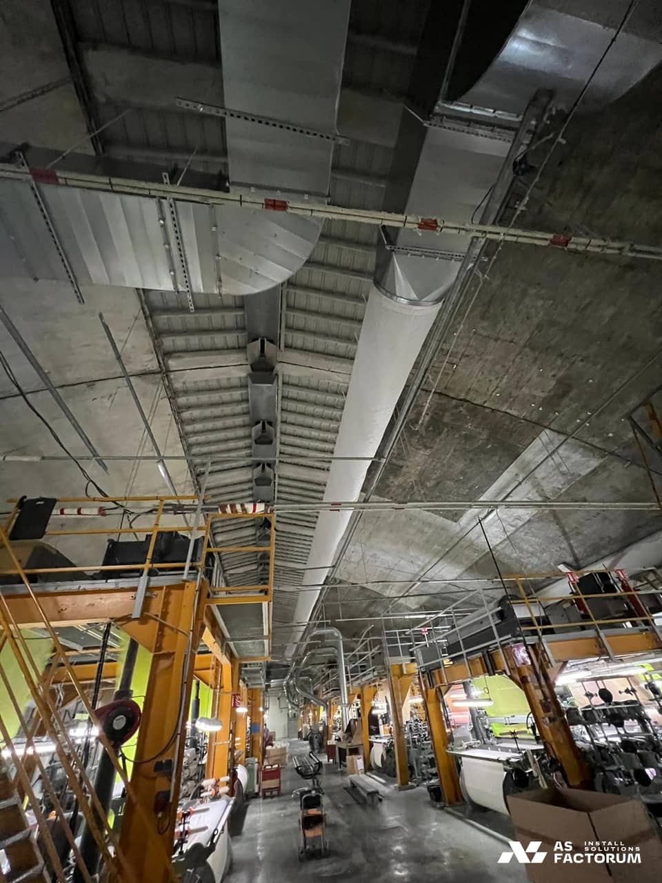 Sheet-metal ventilation ducts and a white fabric duct under a production hall ceiling