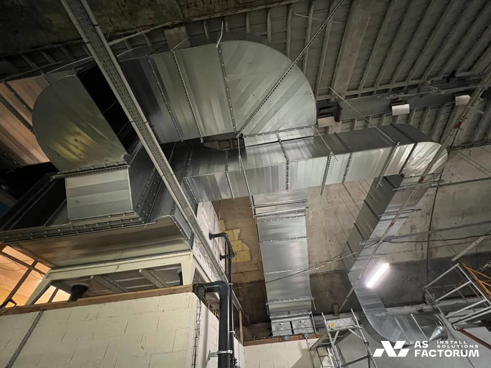 Branching rectangular galvanised duct with elbows rising from a white unit towards the ceiling