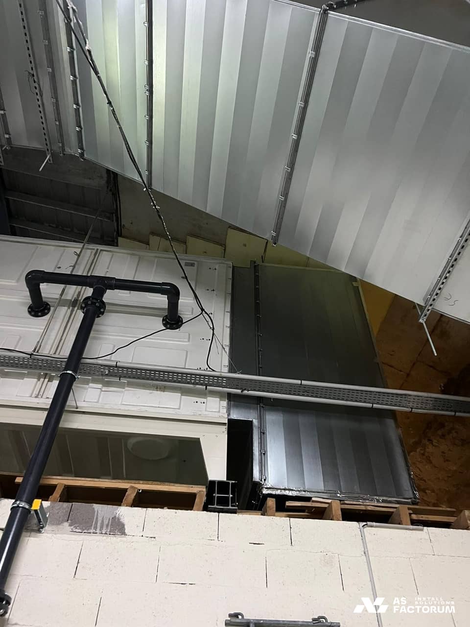 Duct and white unit seen from below, with a black pipe crossing the frame