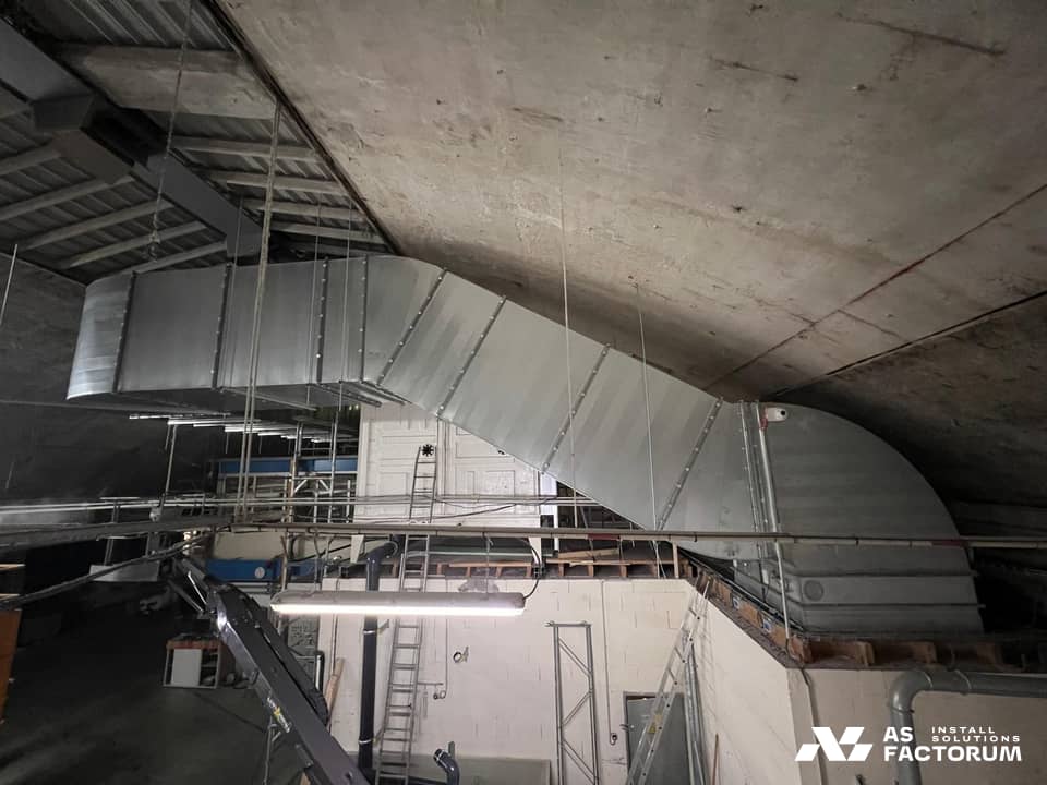 Sloping galvanised duct run with flanged joints, hanging beneath the vaulted concrete ceiling