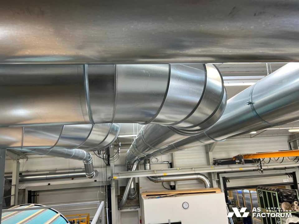 Large galvanised ducts and bends under the roof, above the equipment in the hall