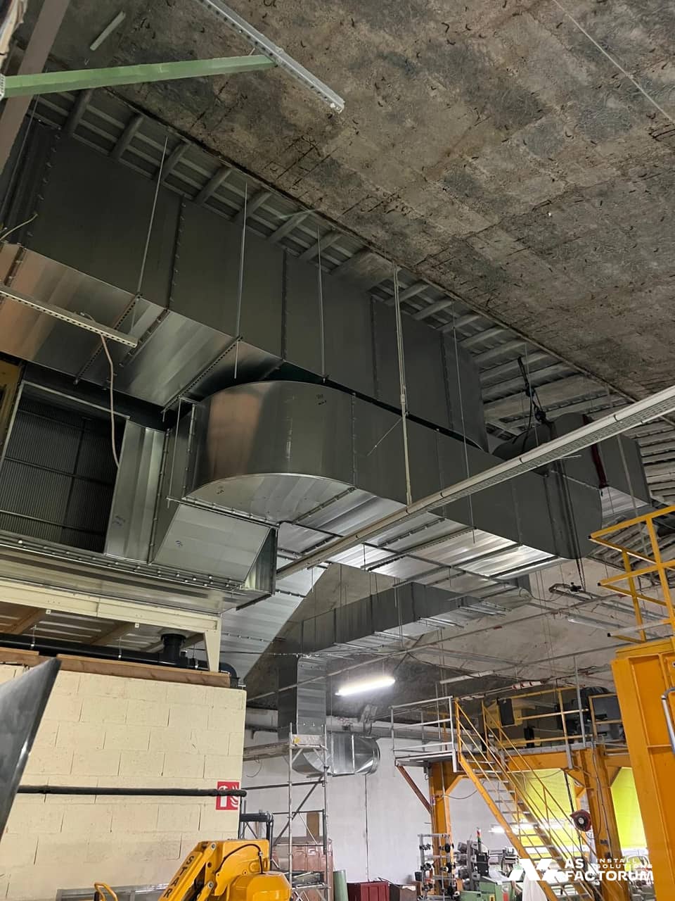 Large rectangular ducts under a concrete ceiling above a white unit and scaffolding