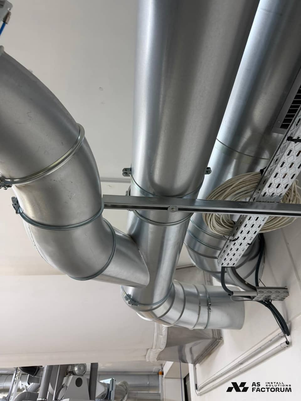 Round ducts mounted overhead beside a cable tray under the hall roof