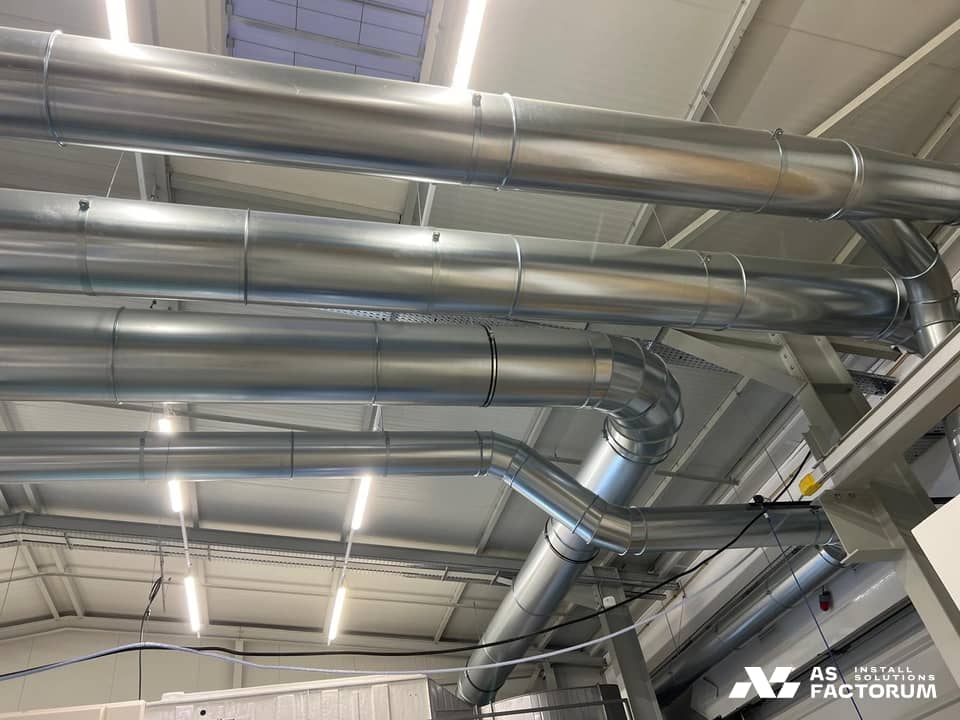 Parallel round galvanised ducts suspended along the ceiling of a hall