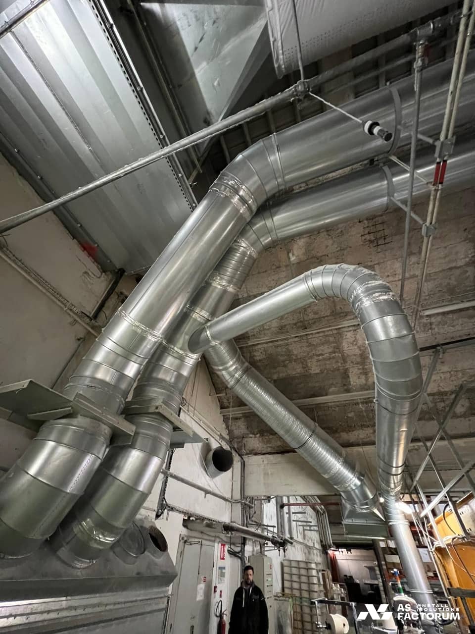 Spiral ducts with elbows branching from a unit, with a person standing below