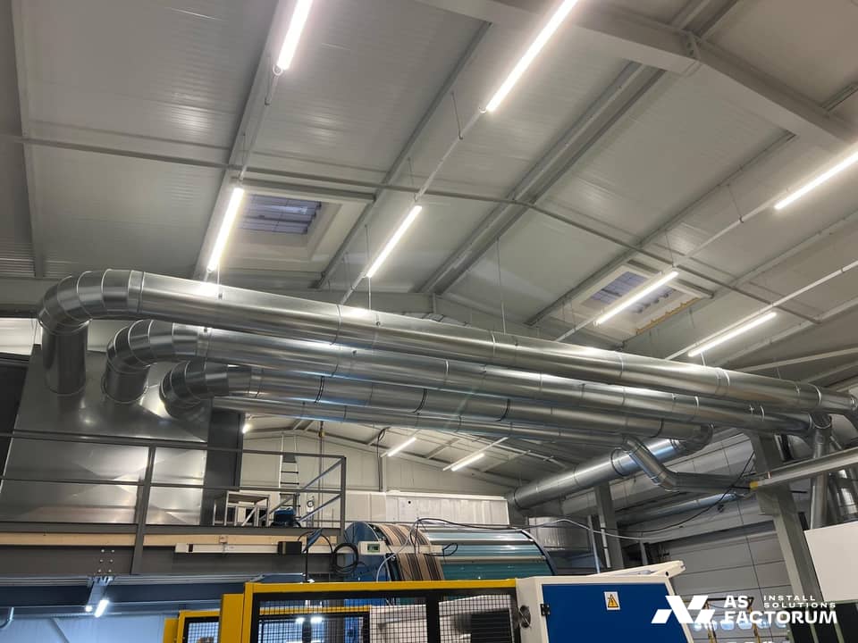 Spiral galvanised ducts mounted side by side in a high-ceilinged hall