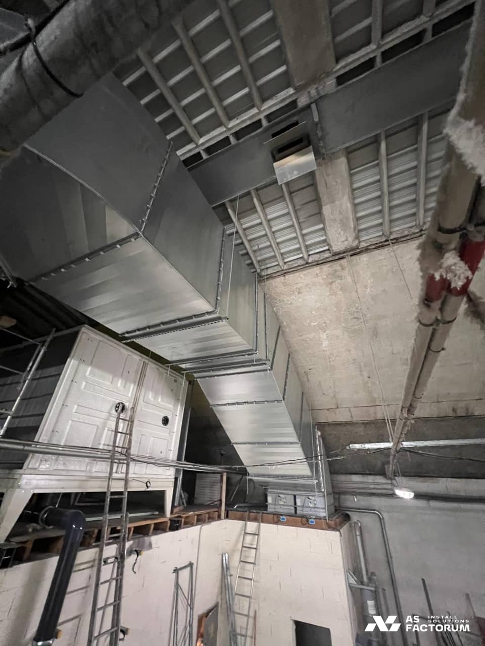 Rectangular galvanised ducts above a white unit, beneath a concrete vault and steel beams