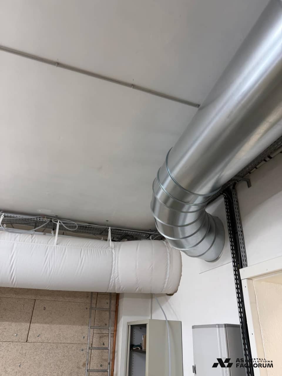 Round galvanised duct elbow next to a white fabric duct