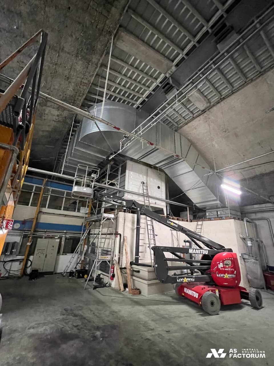 Red boom lift in front of a white unit, with galvanised ducts suspended under the hall vault