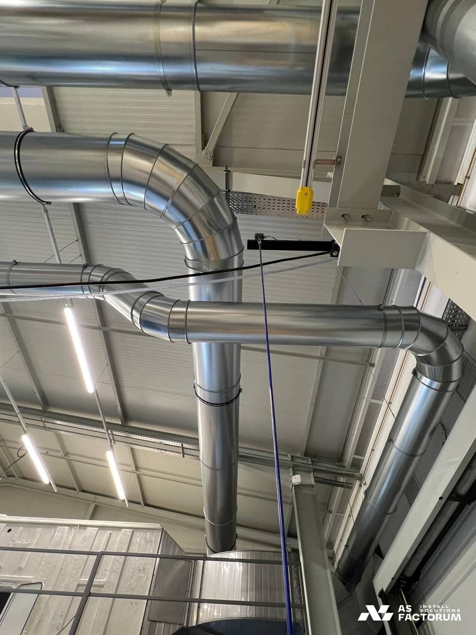 Y-shaped junction of round galvanised ducts dropping from the ceiling on a steel frame