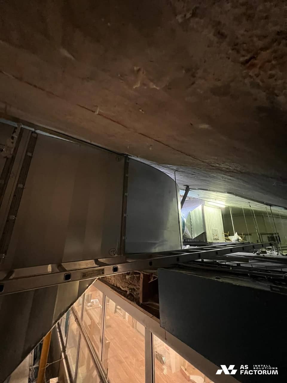 Dark concrete ceiling with ventilation ducts and a ladder leaning below