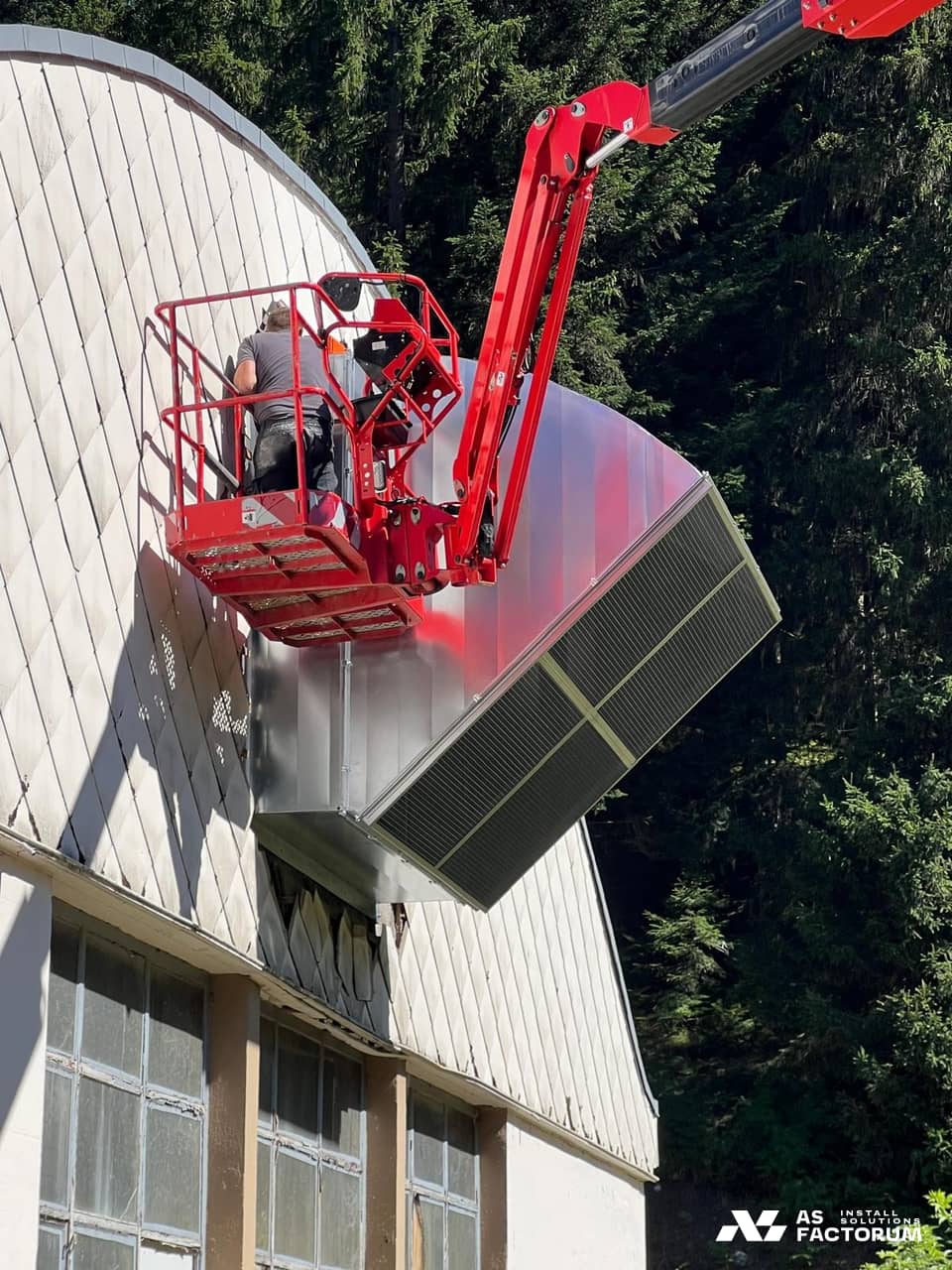 Louvred unit raised by a red boom lift, with a worker beside it